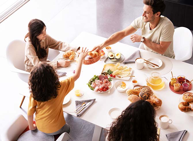 Familie sitzt am Frühstückstisch und isst frische Brötchen