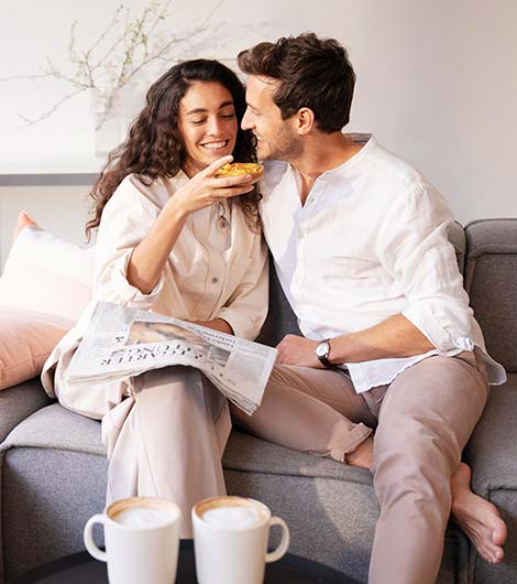 Pärchen sitzt auf der Couch, Frau hält belegtes Brötchen in der Hand