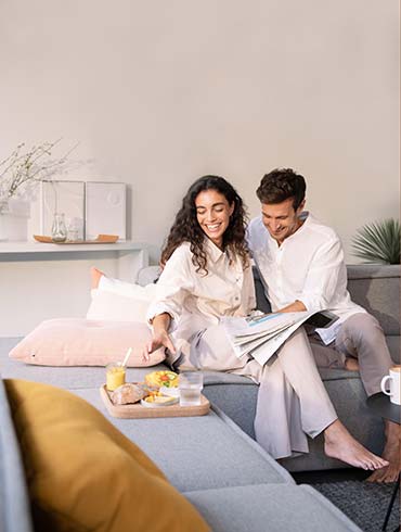 Zwei Personen lachen und frühstücken frische Brötchen auf dem Sofa