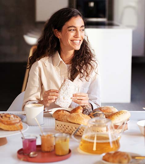 Lachende Frau frühstückt frische Brötchen und süße Backwaren vom Frühstückslieferdienst